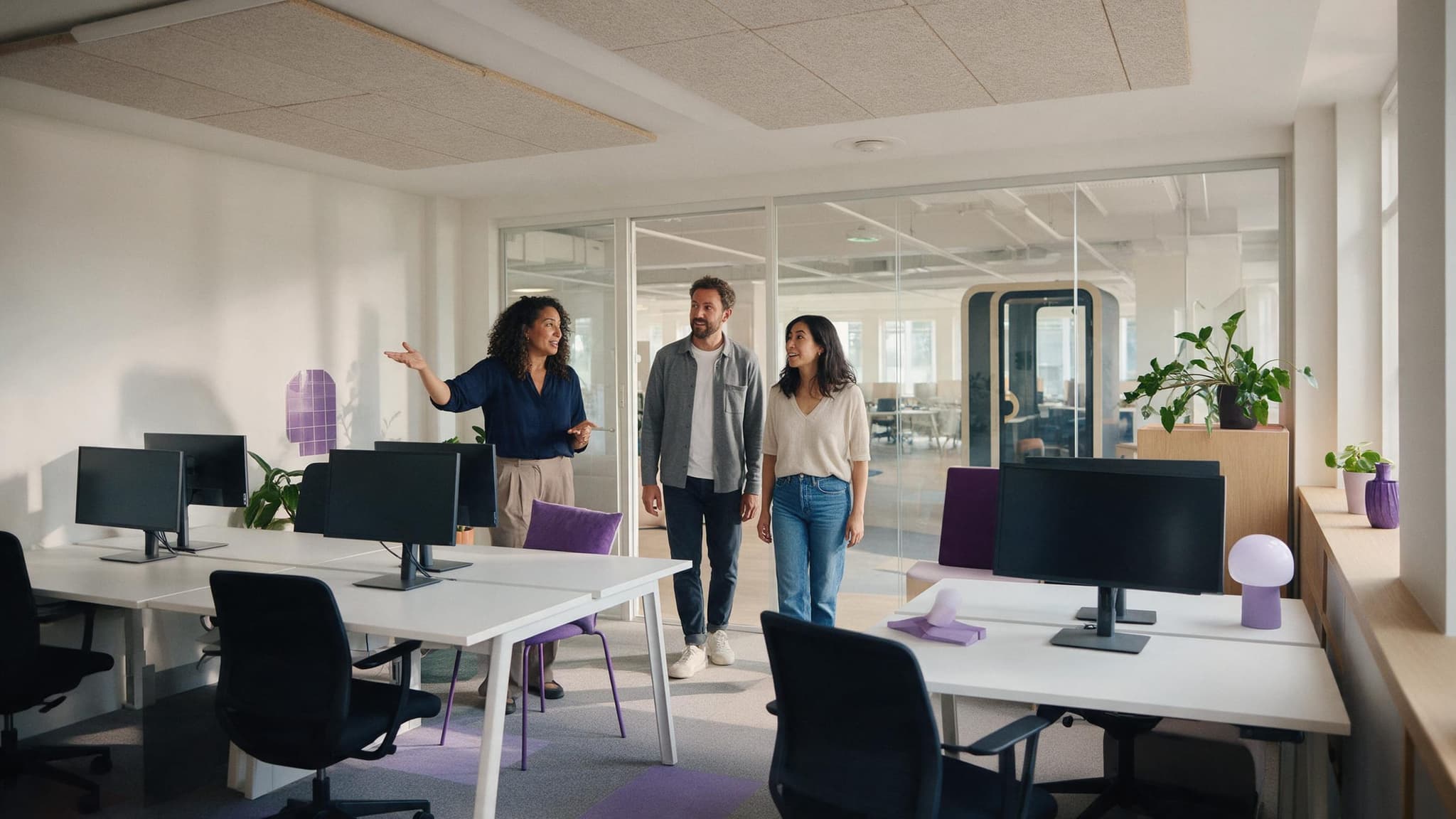 A community manager shows two founders around a flexible office floor with desks, monitors and a phone booth.
